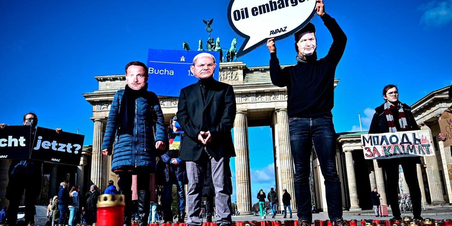   Activists wearing masks with the likenesses of Chancellor Scholz, Finance Minister Lindner, left, and Economics Minister Habeck and holding a sign reading "Oil embargo?" demonstrate at the Brandenburg Gate in favor of an embargo on Russian oil and gas in Berlin, Germany, Friday, April 8, 2022. (Fabian Sommer/dpa via AP)  MAS141